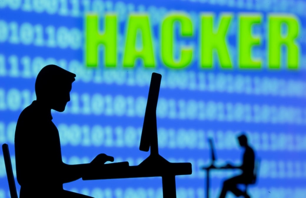 Photo d'illustration montrant des hommes travaillant sur des ordinateurs devant un code binaire et le mot "hacker"
