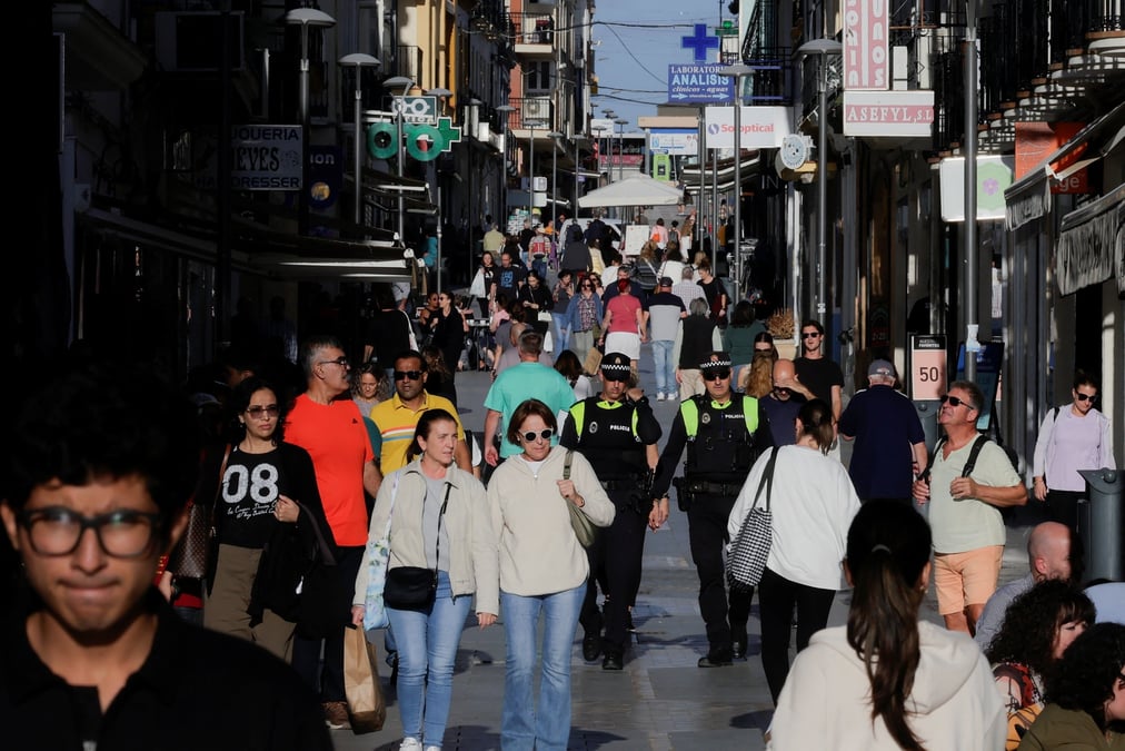 People walk along la bola shopping street during sunset in ronda