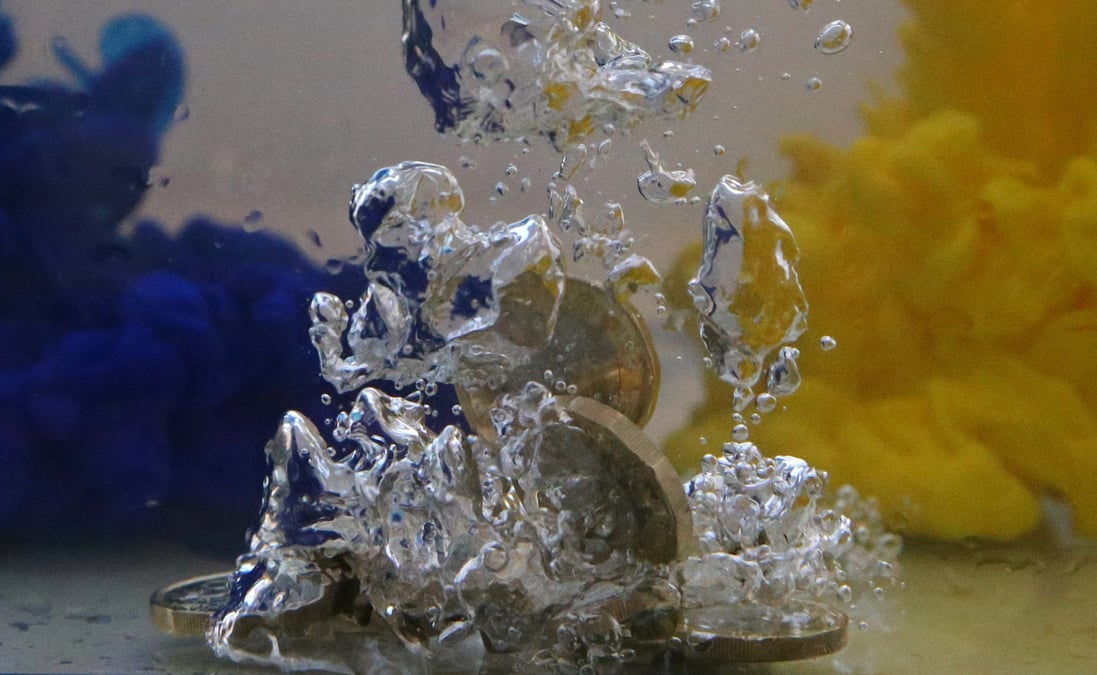 Des pieces de monnaie en livres sterling dans de l'eau aux couleurs du drapeau de l'union europeenne