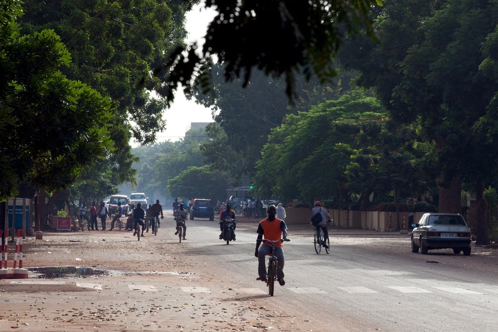 Des personnes se deplacent a velo et a moto dans une rue de ouagadougou