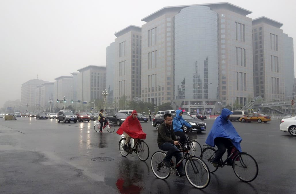 Residents ride their bicycles next to vehicles traveling along the chang'an avenue amid rainfalls on a hazy day in central beijing