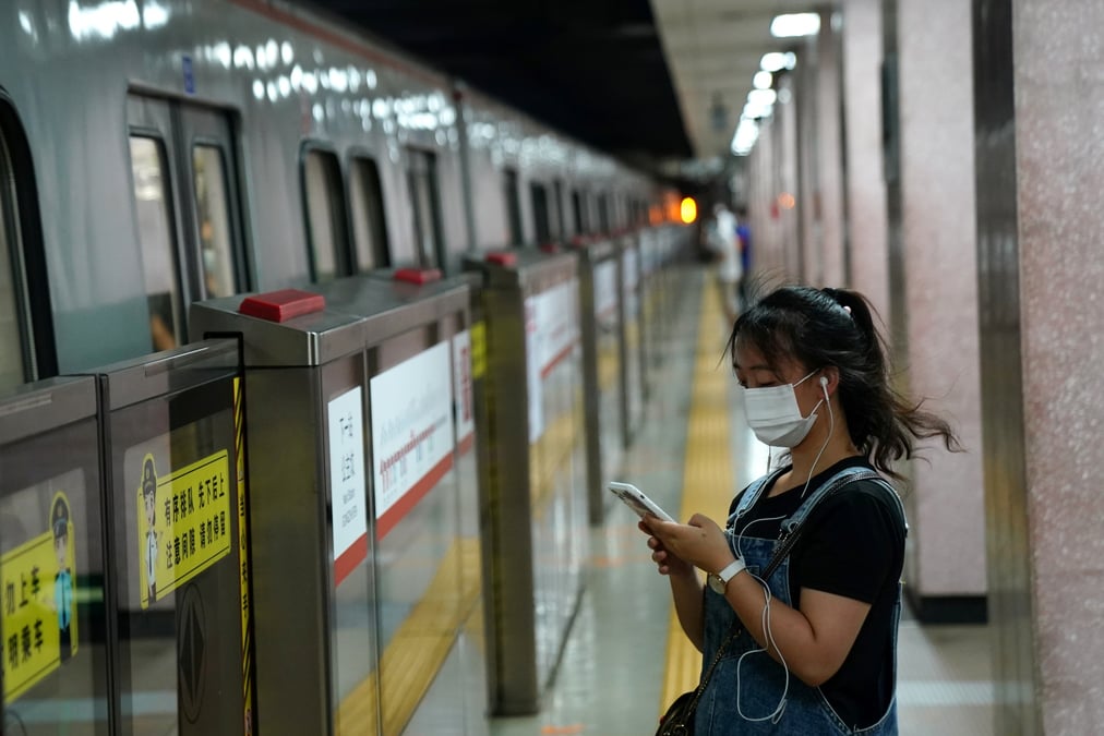 Une femme portant un masque regarde son smartphone en attendant le metro a pekin