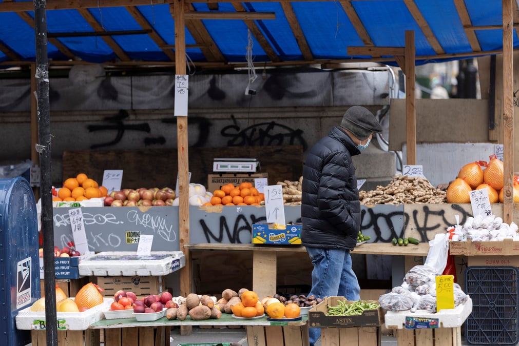 Photo d'une personne qui passe devant un etal vendant des fruits et legumes a manhattan