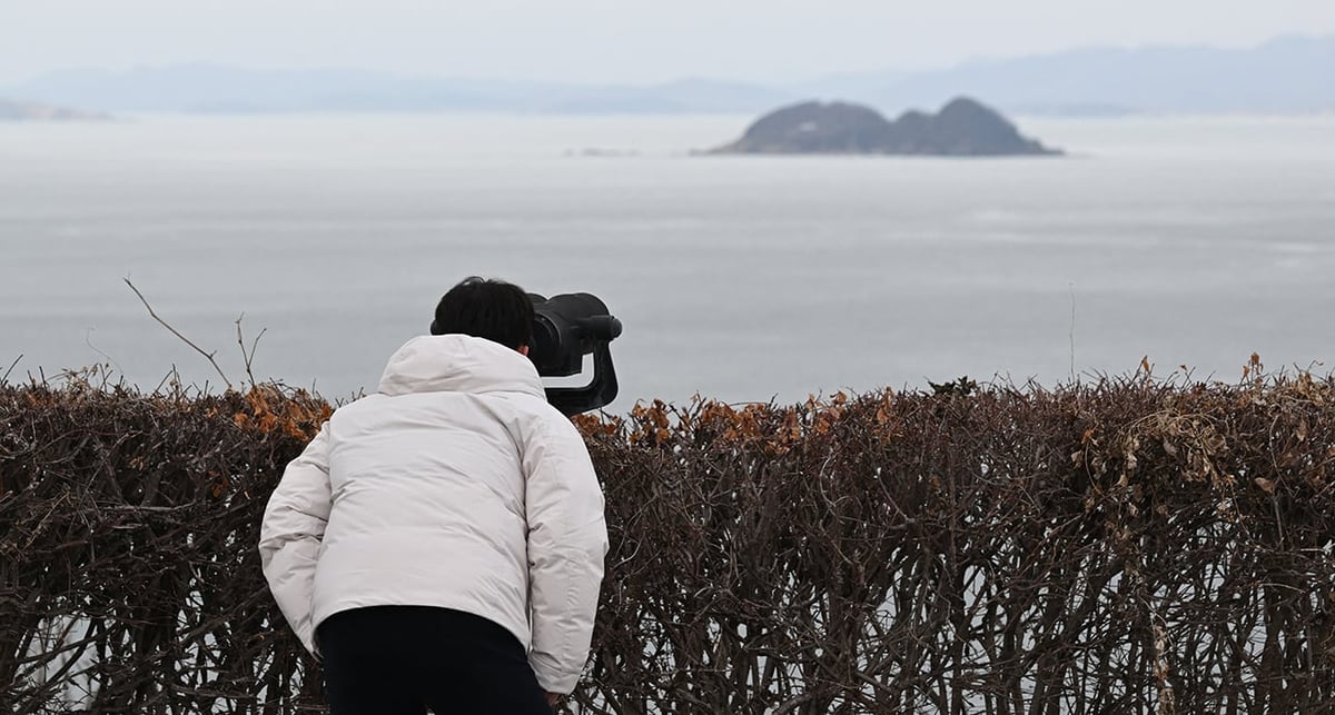 Un homme observe la côte nord-coréenne avec des jumelles depuis l'île sud-coréenne de Yeonpyeong, près de la frontière maritime nord-coréenne, le 8 janvier 2024.
