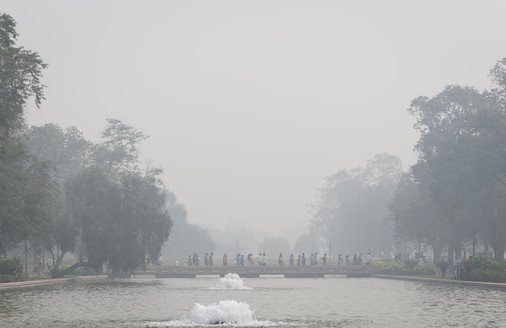 Des personnes marchent sur un sentier au-dessus d'un etang au milieu d'un lourd smog a new delhi
