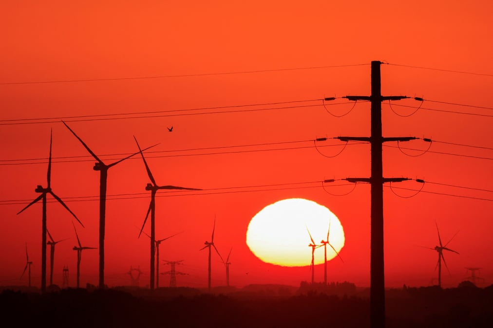 Des eoliens et des pylones electriques sont photographies au lever du soleil