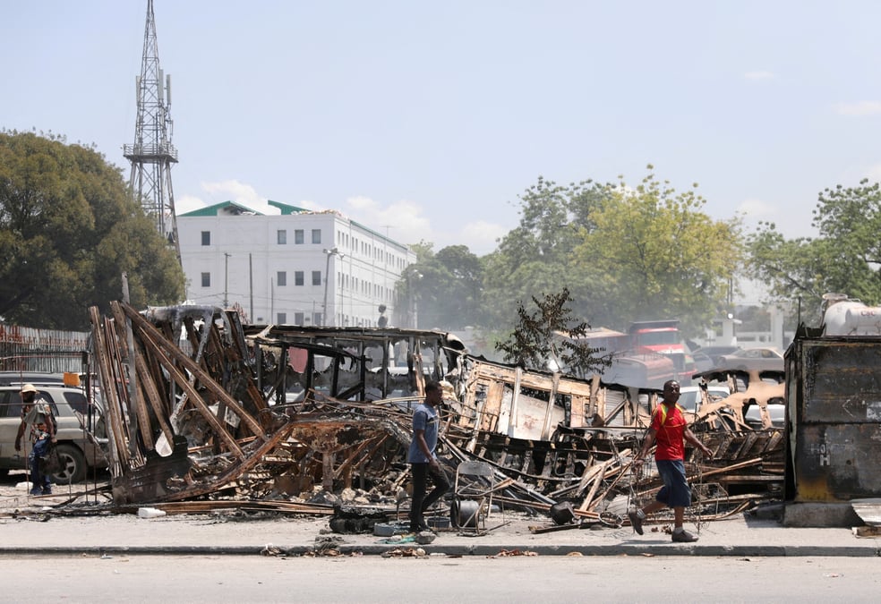 Des gens passent devant les restes de vehicules incendies par des gangs, a port-au-prince