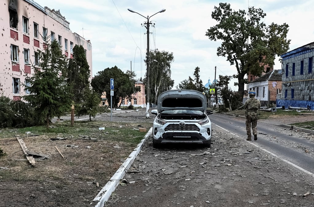 A ukrainian serviceman patrols a street next to damaged buildings in the town of sudzha