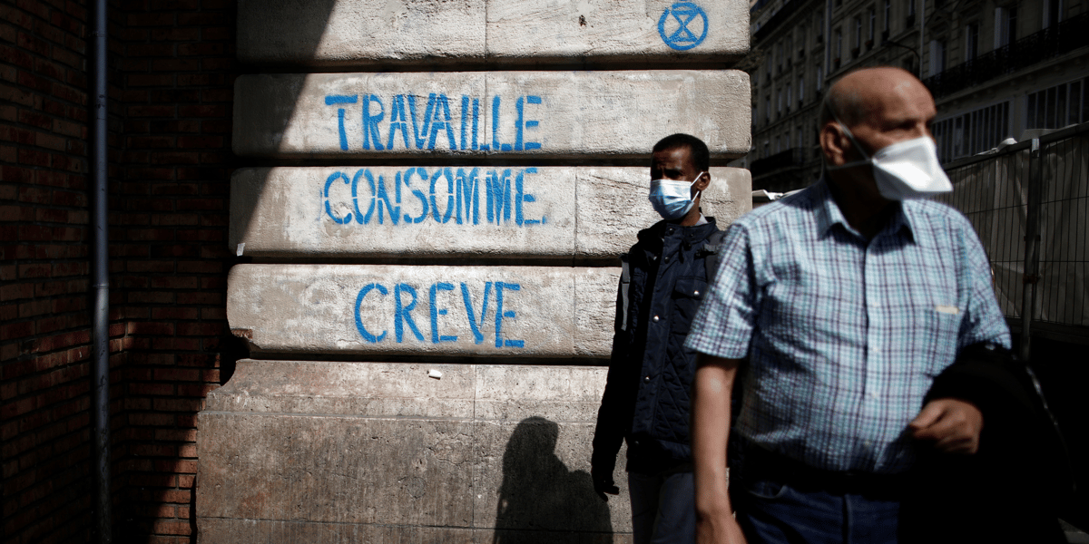 Coronavirus : deux personnes portant un masque passent devant un slogan disant : "Travaille, consomme, crève" (à Paris)