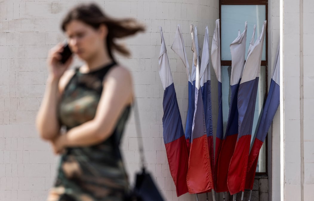 Une femme parle au telephone en passant devant des drapeaux nationaux russes a koursk