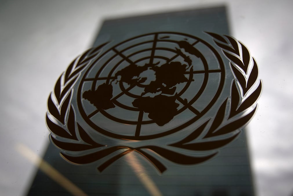 Le batiment du siege des nations unies se reflete dans une fenetre avec le logo de l'onu au premier plan, new york