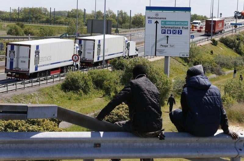 Two migrants sit on a guardrail which overlooks the road that lorries take to reach the channel tunnel crossing in calais