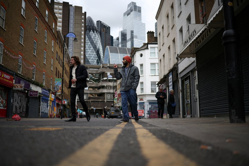 Des personnes passent devant des magasins, avec le quartier financier de la city de londres en arriere-plan