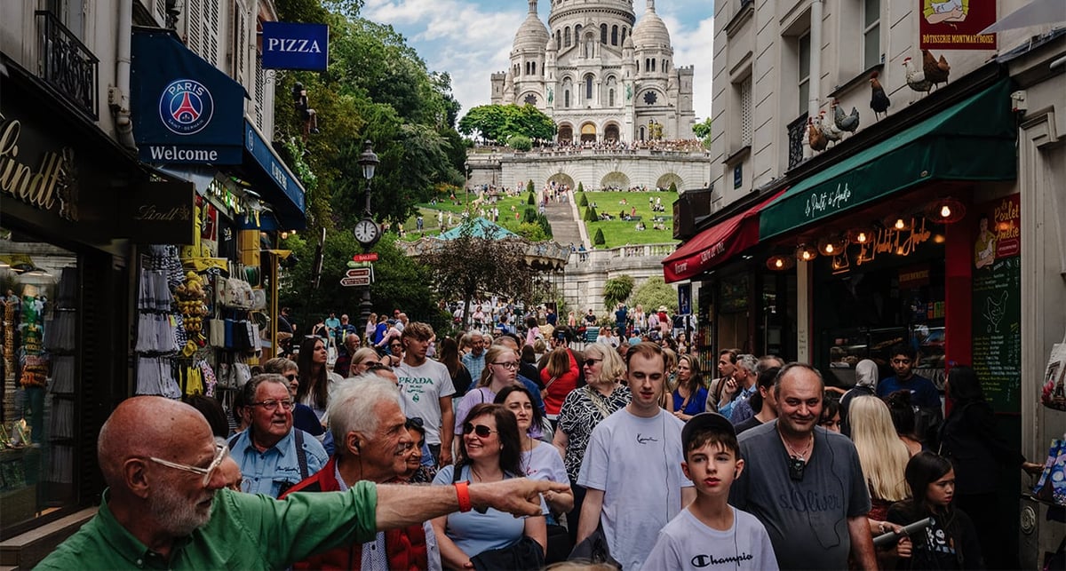 Des touristes se promènent le long de la rue Steinkerque avec la basilique du Sacré-Cœur sur la butte Montmartre en arrière-plan, à Paris, le 1er août 2025.