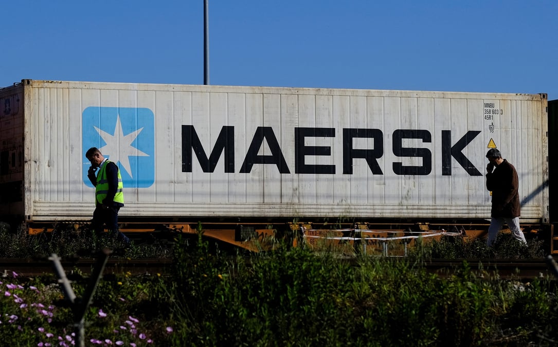 Des travailleurs parlent sur leur telephones portables, alors qu'un conteneur maersk est transporte par un train, pres du port de barcelone