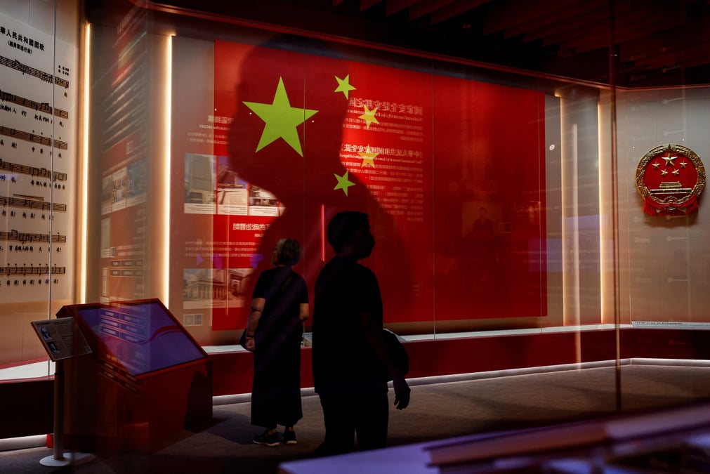 Des visiteurs passent devant le drapeau national chinois et l'embleme a la galerie d'exposition de la securite nationale, avant le 75e jour national de la chine a hong kong