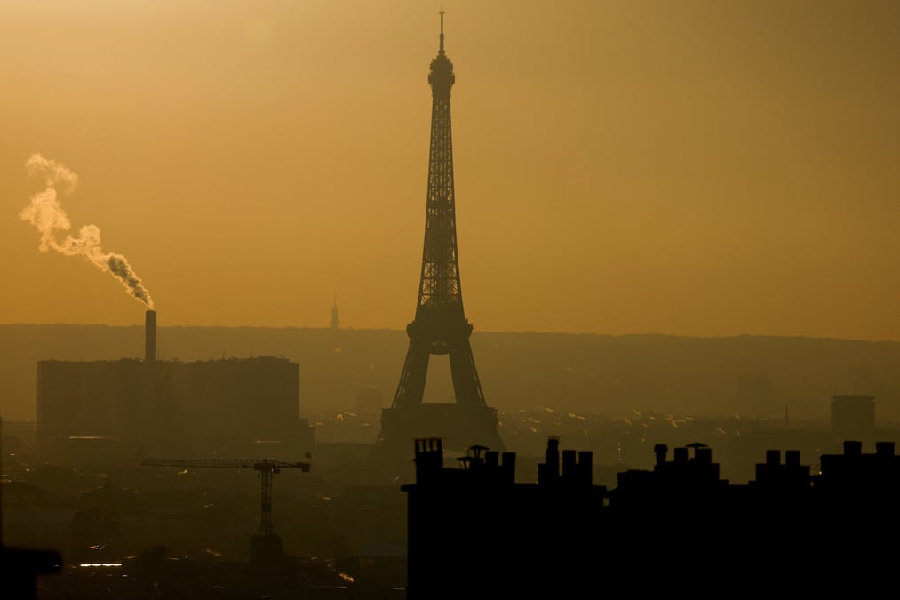 Une vue d'ensemble montre la tour eiffel et la vapeur qui s'echappe des cheminees dans l'horizon de paris