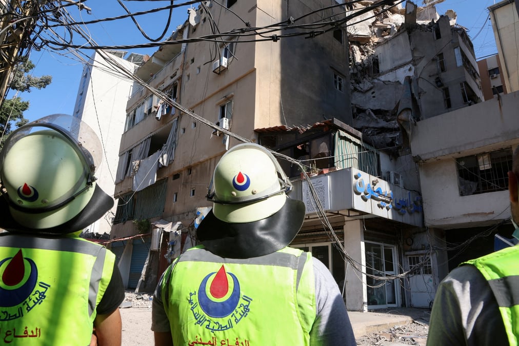 Des membres de la defense civile se tiennent pres d'un batiment endommage au lendemain d'une frappe israelienne a beyrouth