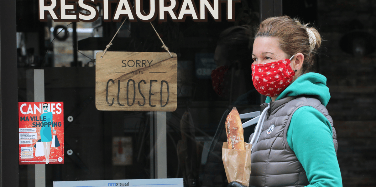 Fermeture commerce restaurant. Une femme portant un masque et une baguette passe devant un restaurant fermé à cause de l'épidémie de coronavirus, le 16 avril 2020 à Cannes