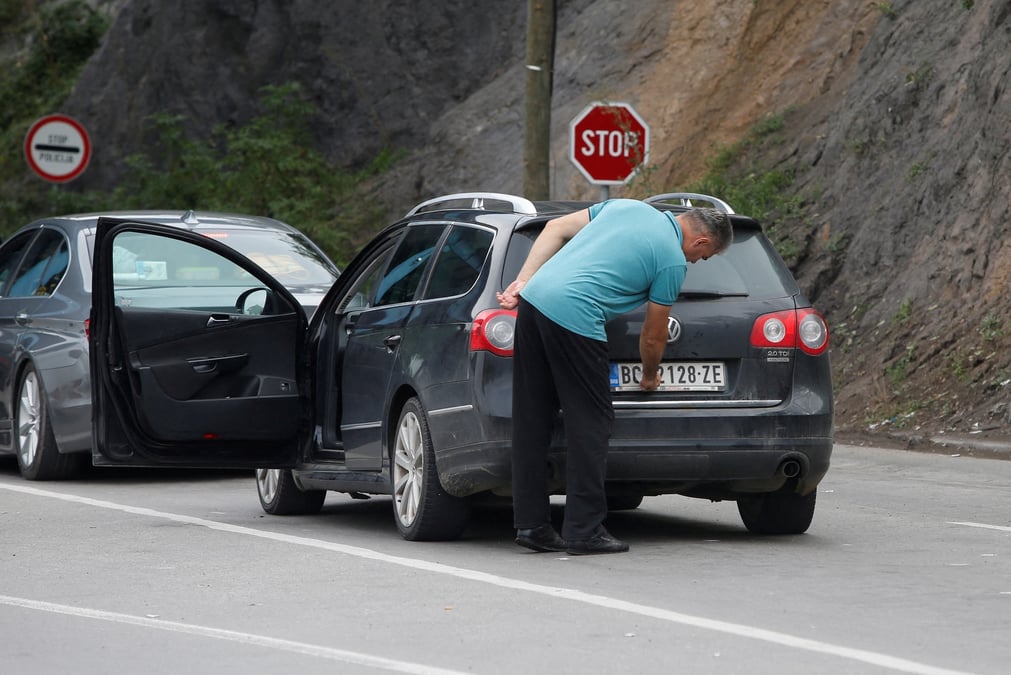 Photo d'archives d'un conducteur retirant un autocollant couvrant les marquages nationaux sur les plaques de sa voiture au poste frontiere de jarinje