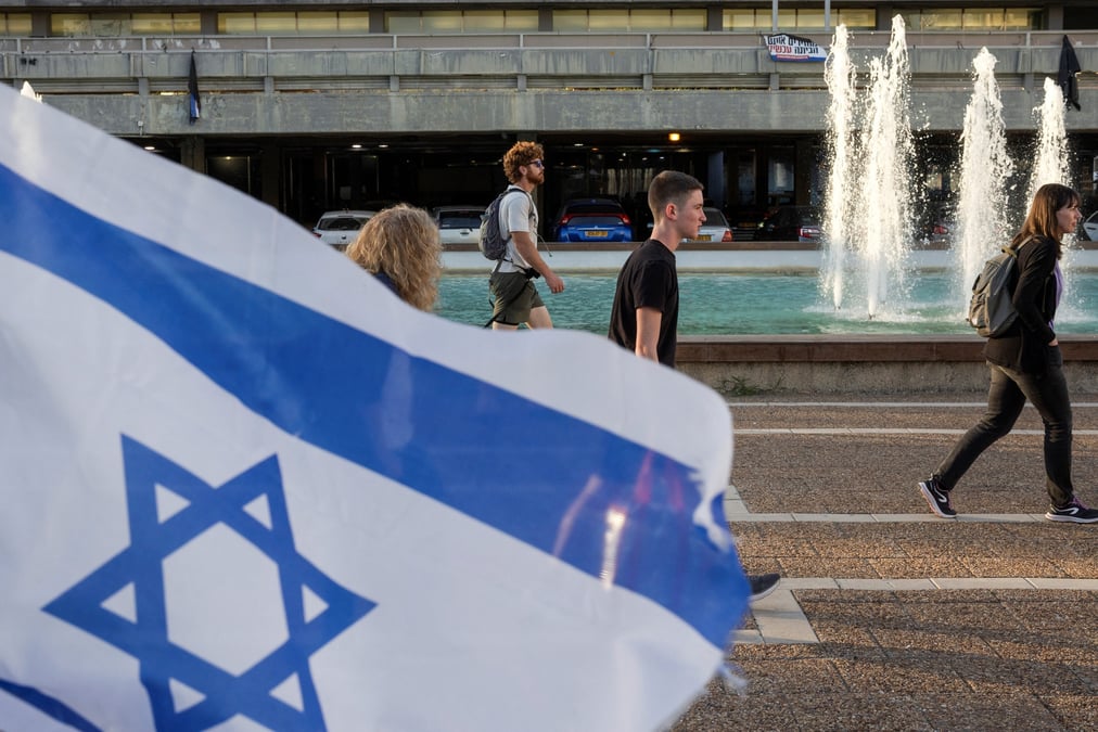 Des personnes passent devant un drapeau israelien a tel aviv
