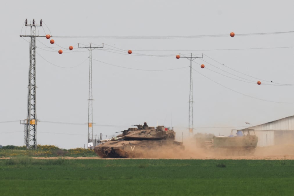 Photo d'un un char israelien qui tire un vehicule blinde de transport de troupes (apc) pres de la frontiere entre israel et gaza