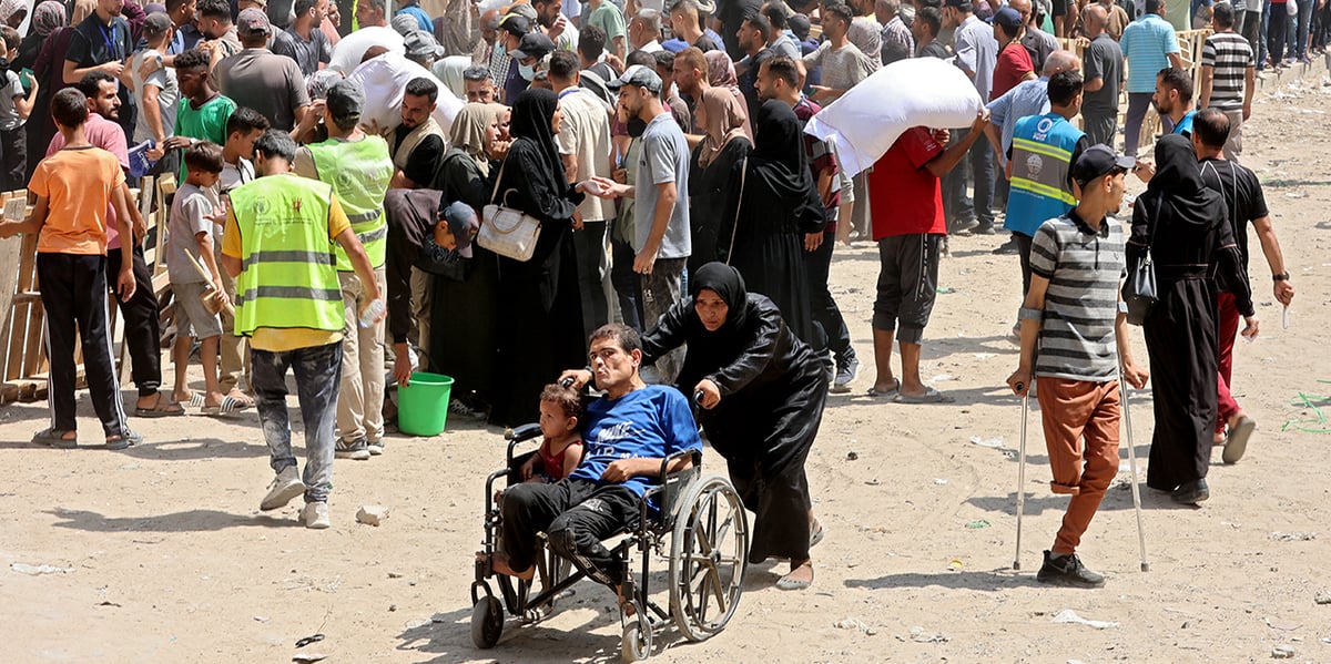 Une femmes pousse un enfant et un homme dans un fauteuil roulant pendant une distribution de sacs de farine par l'ONU à Gaza.