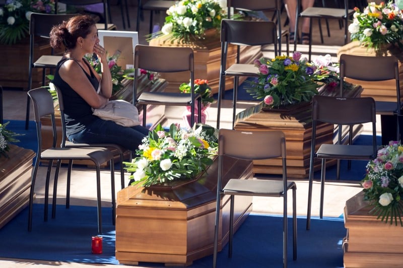 A woman sits next to a coffin to pay her respects as she attends a funeral for the earthquake victims inside a gym in ascoli piceno