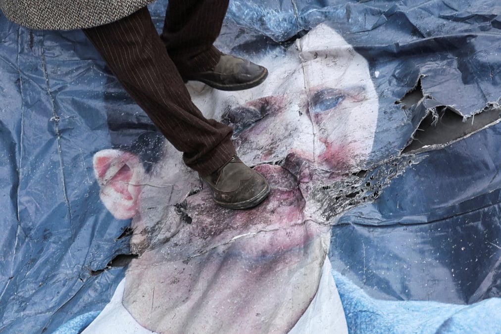 Un homme marche sur une affiche de bachar al-assad dans le centre-ville de damas, en syrie