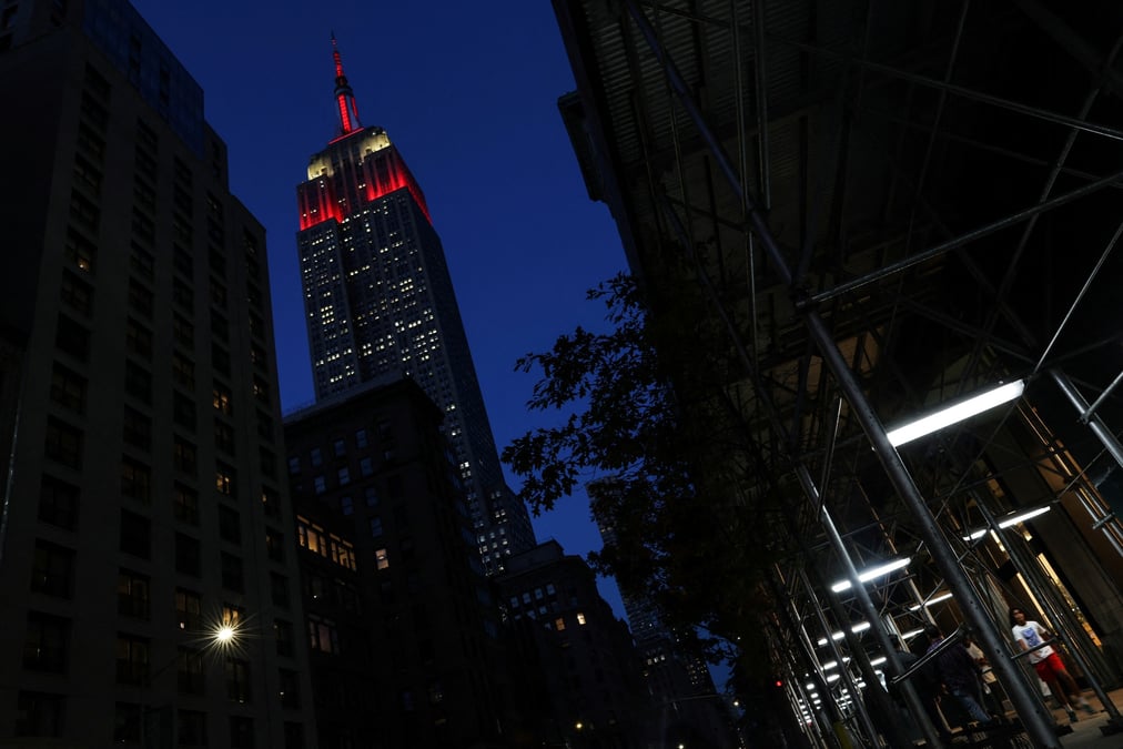 L'empire state building est illumine en rouge alors que des personnes marchent dans le quartier de midtown a new york