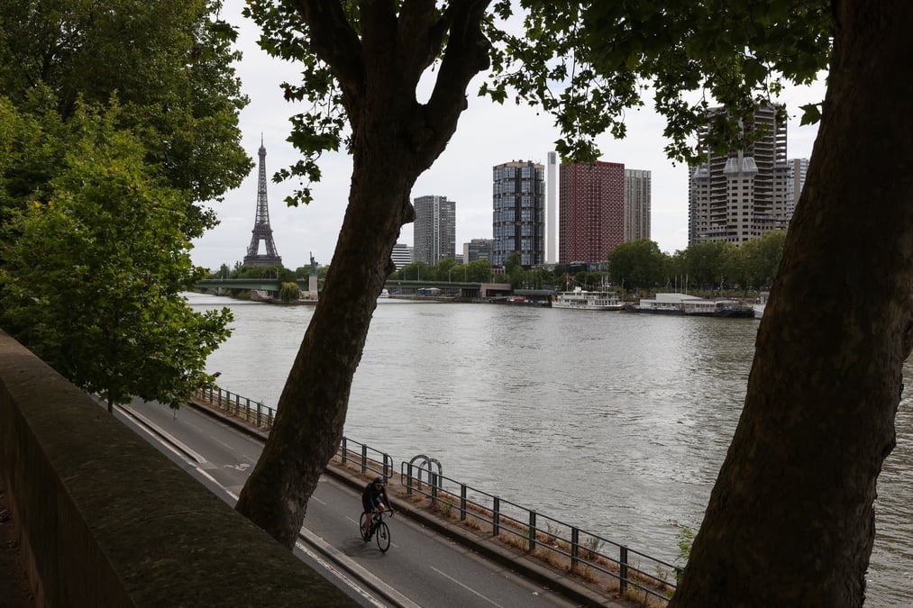 Un homme roule a velo sur les rives de la seine avec la tour eiffel en arriere-plan