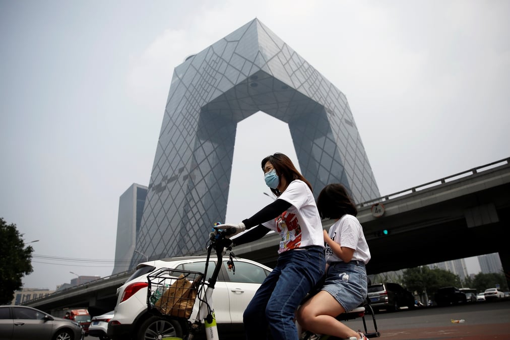 Chine : une femme portant un masque roule en vélo électrique devant le siège de la Télévision centrale de Chine à Pékin le 16 juillet 2020