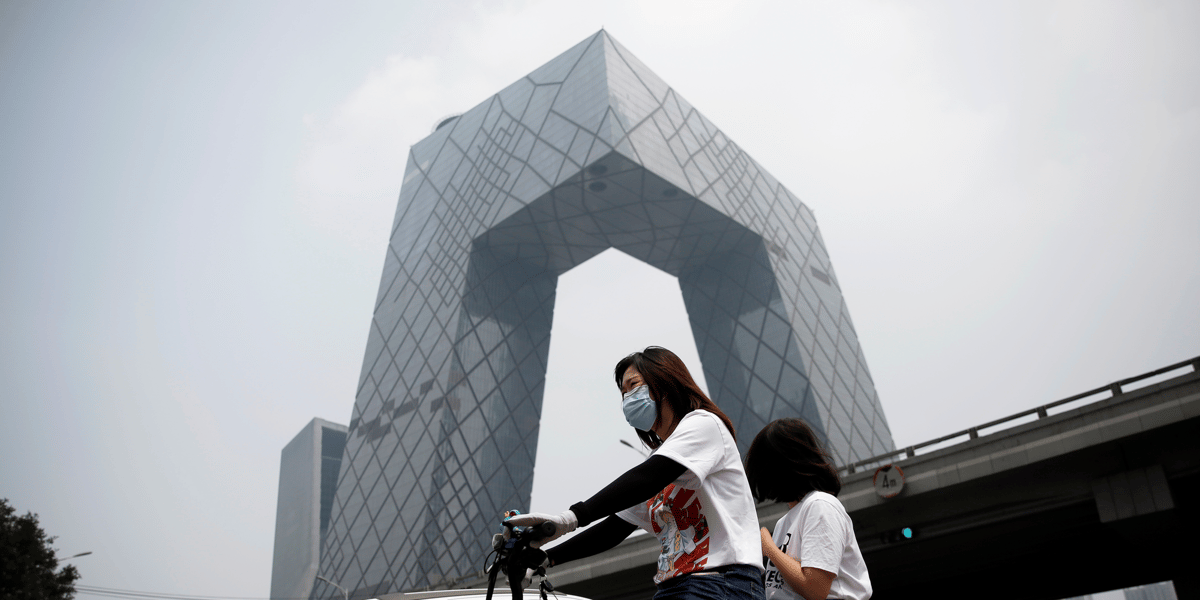 Chine : une femme portant un masque roule en vélo électrique devant le siège de la Télévision centrale de Chine à Pékin le 16 juillet 2020