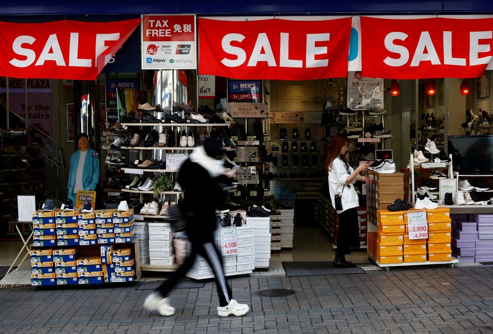 Un passant passe devant un magasin de detail affichant des bannieres "sale" a tokyo