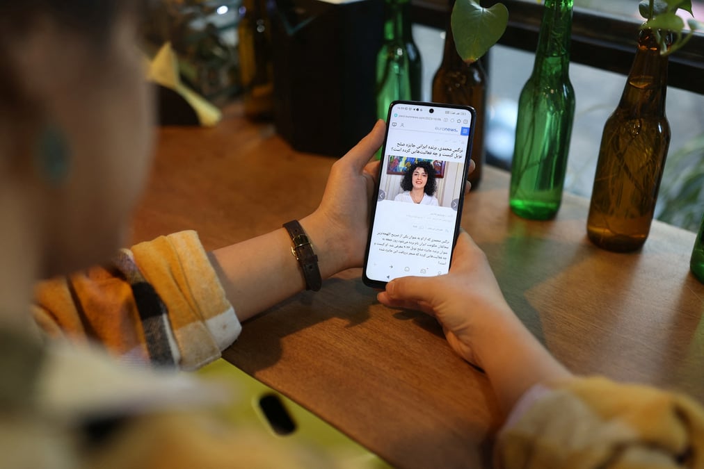 Une femme iranienne regarde sur son telephone portable la nouvelle que la militante iranienne des droits de l'homme narges mohammadi a gagne le prix nobel de la paix, dans un cafe a teheran