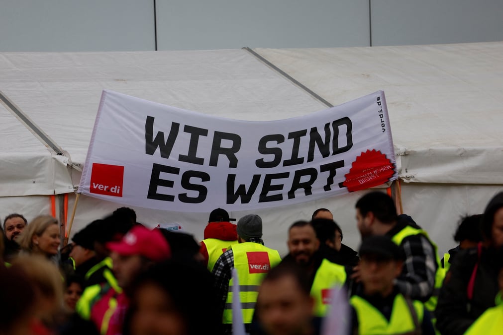 Photo des employes qui tiennent une banderole "nous en valons la peine" lors d'une greve aux aeroports de francfort, munich, stuttgart, hambourg, dortmund, hanovre et breme
