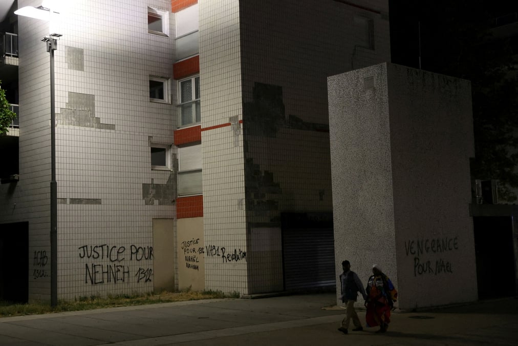 Des habitants passent devant des phrases ecrites sur les murs des immeubles de nanterre, le quartier du jeune de 17 ans tue par un policier lors d'un controle routier
