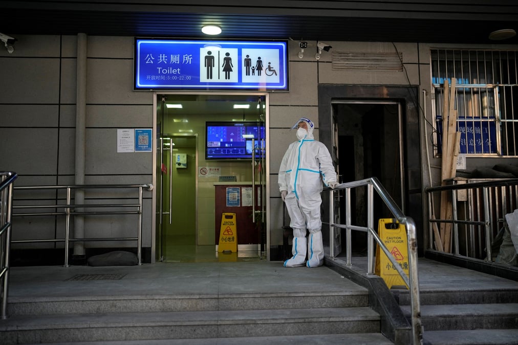 Un travailleur en combinaison de protection surveille l'exterieur d'une toilette publique a shanghai