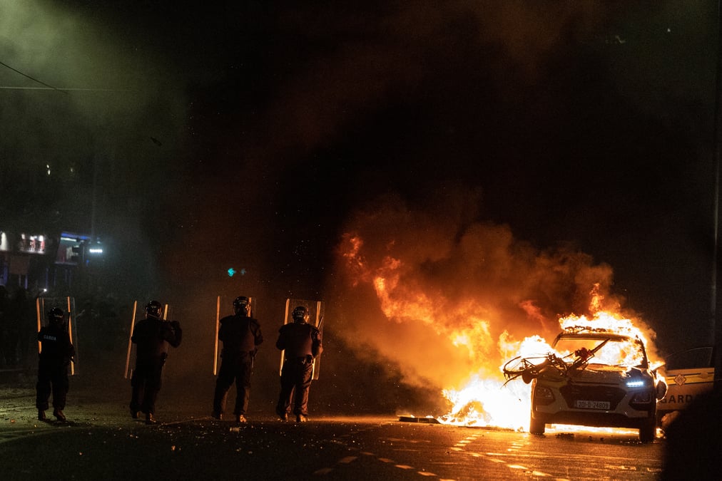 Des policiers font face a des manifestants a cote d'une voiture de police en feu, a la suite d'une attaque au couteau survenue plus tot dans la capitale irlandaise