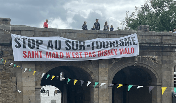 Dimanche 16 juillet au matin, une large banderole a été déroulée en haut des remparts de la vieille ville de Saint-Malo (Ille-et-Vilaine) pour dénoncer le surtourisme. (@SoLeNoenLess)
