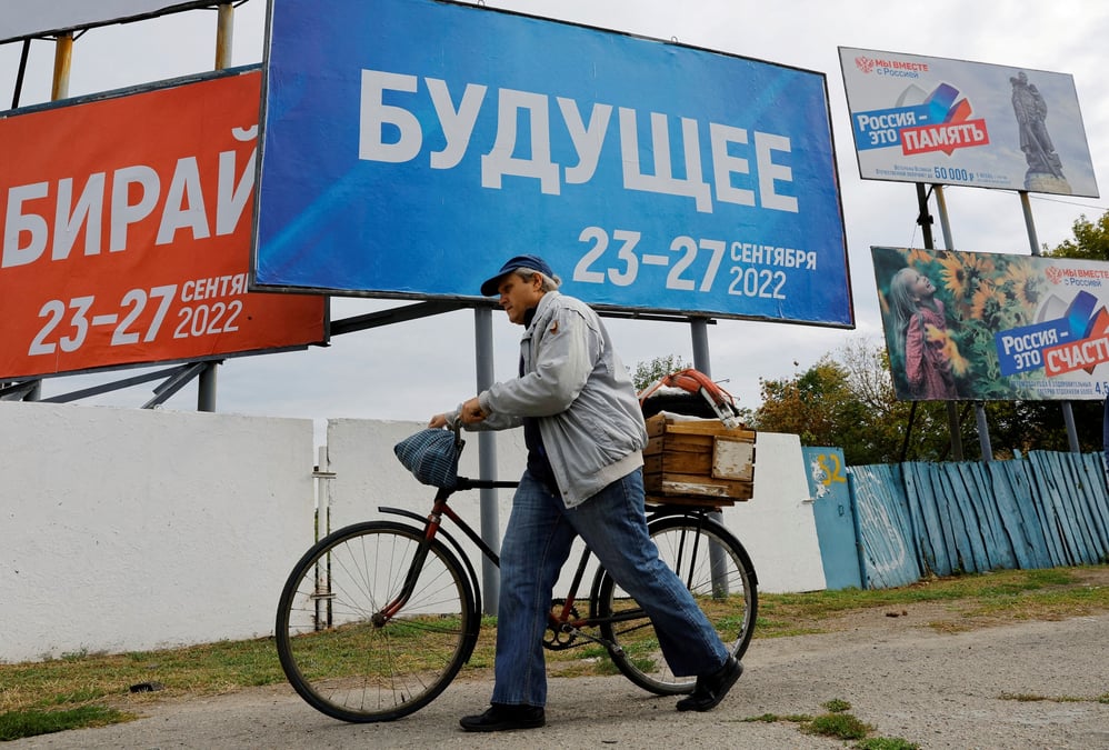 Un homme avec un velo devant des panneaux au sujet d'un referendum sur le rattachement a la russie des regions d'ukraine controlees par la russie