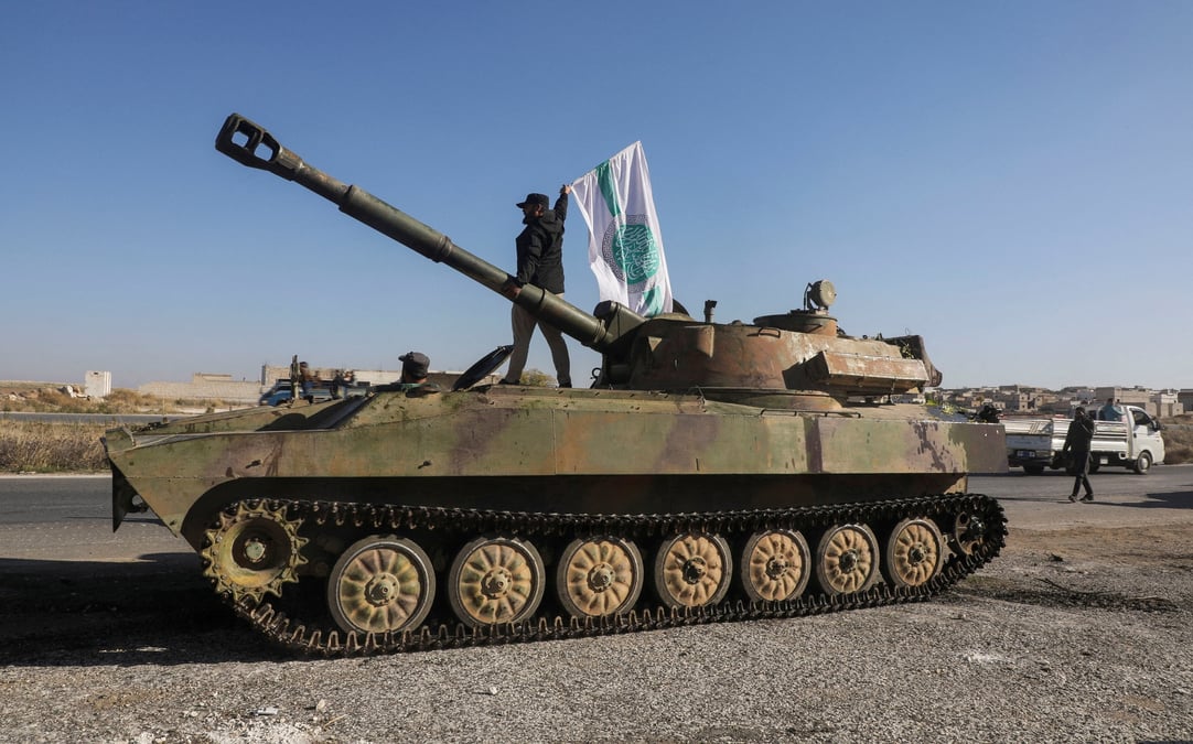 Un combattant rebelle se tient au-dessus d'un vehicule militaire et porte le drapeau de hayat tahrir al-sham a saraqeb