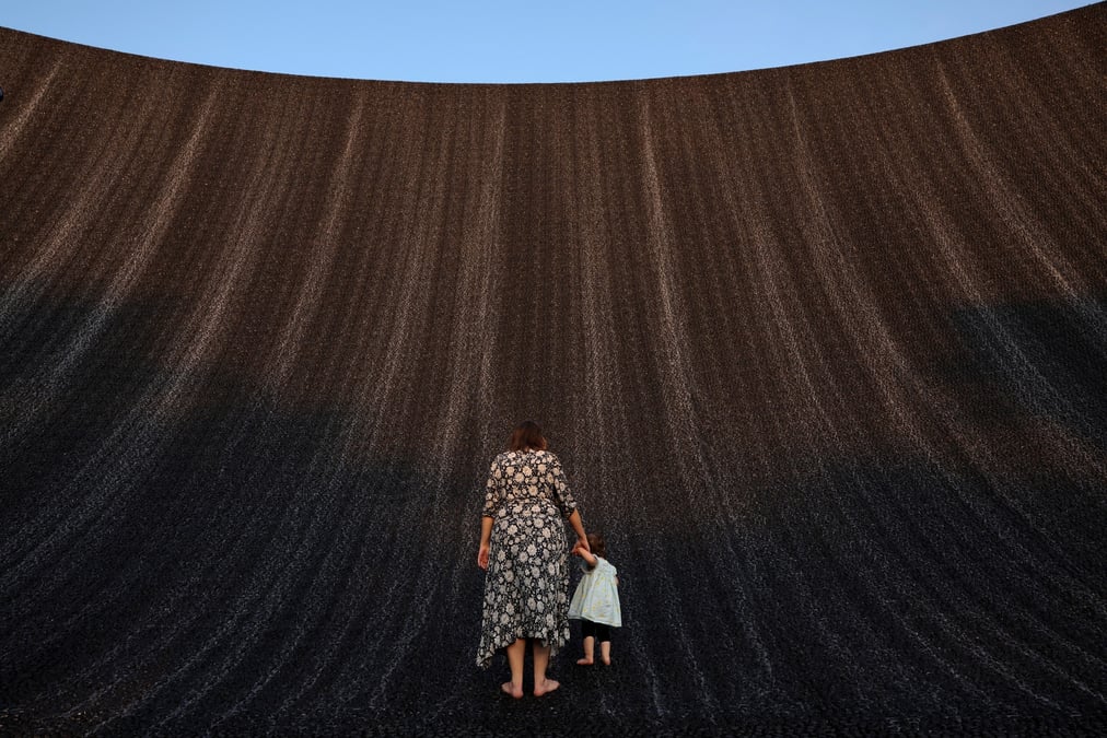 Une femme tient la main d'un bebe alors qu'ils profitent tous deux de la cascade de l'expo a la cop28, a dubai