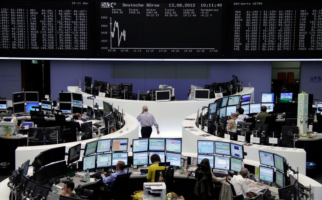 Des courtiers sont assis a leurs bureaux devant le tableau du dax a la bourse de francfort