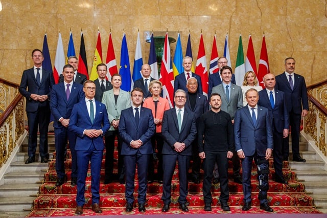 Photo de groupe de responsables politiques posant sur un escalier décoré, devant une rangée de drapeaux nationaux et européen.