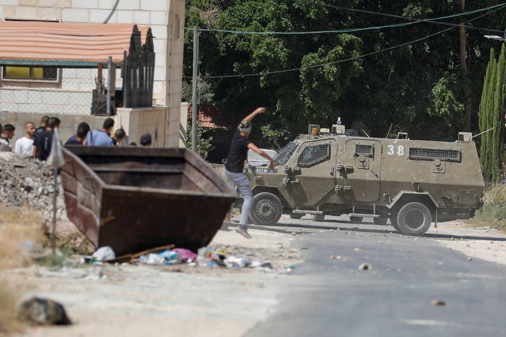 Un palestinien lance une pierre sur un vehicule de l'armee israelienne
