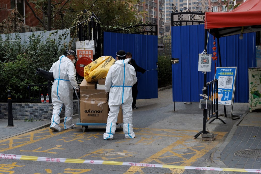 Des hommes portant des combinaisons de protection livrent des colis dans un complexe residentiel qui a ete place en quarantaine a pekin