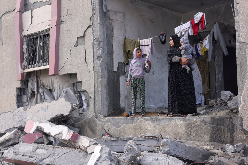 Une palestinienne tient son enfant dans les bras alors qu'elle se tient devant une maison endommagee par les frappes israeliennes, a rafah