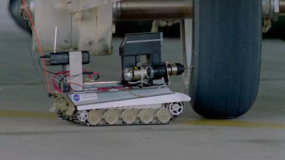 Tire Assault Vehicle (basé sur le modèle réduit de Tigre II) en train de percer un pneu de navette spatiale prêt à éclater sous l'avion d'essai CV-990 LSRA (27 juillet 1995).