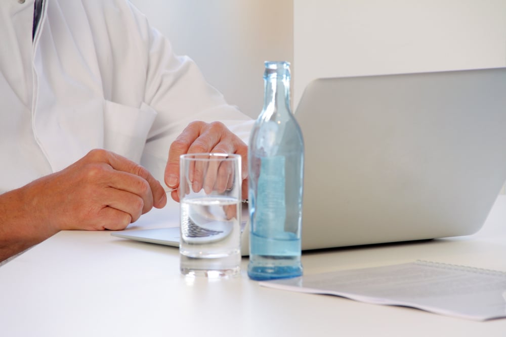 Arzt mit Mineralwasser auf dem Schreibtisch